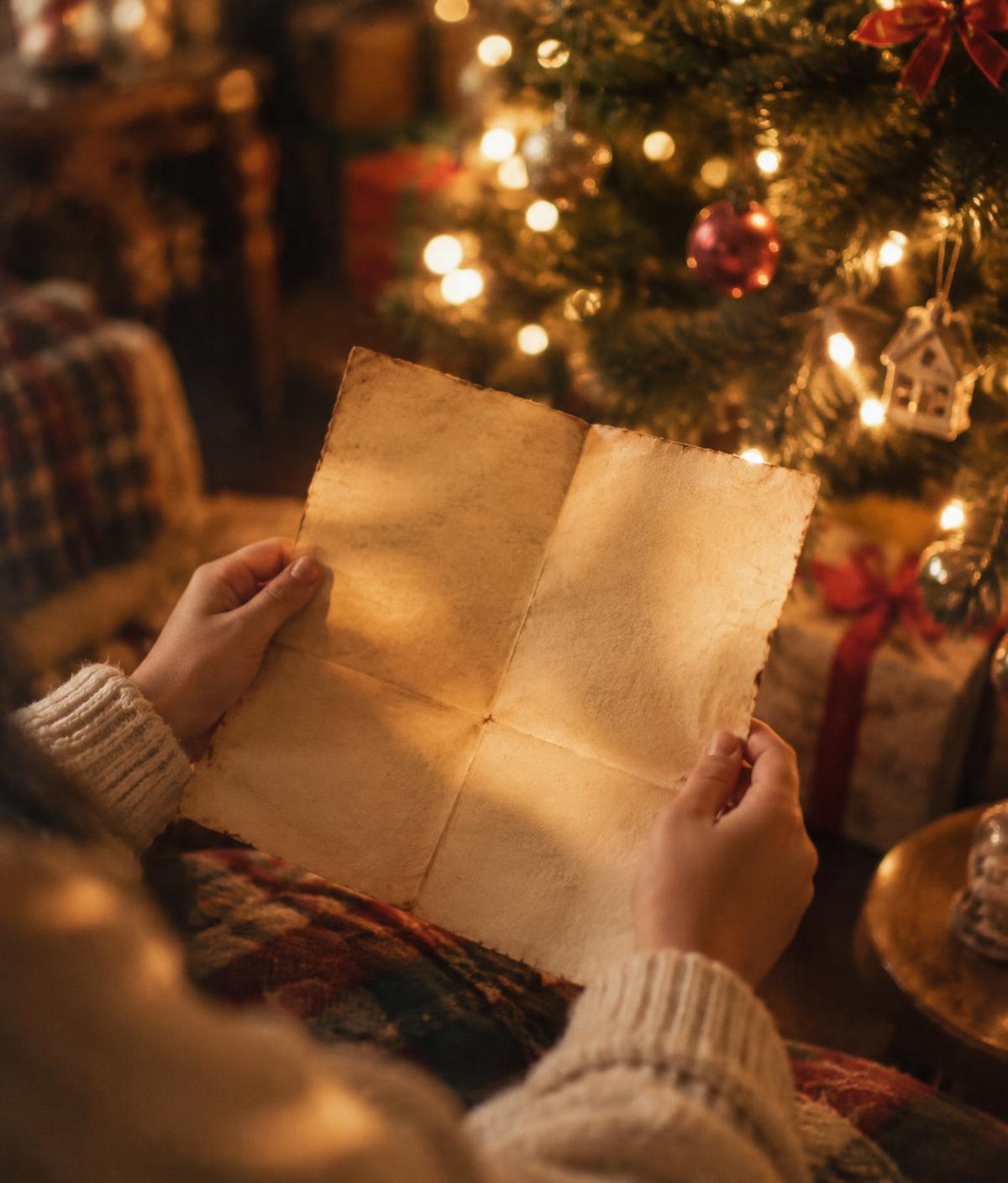 Hands holding a letter beside a Christmas tree
